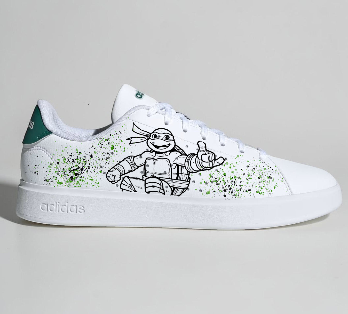 Baskets Adidas blanches personnalisées avec un dessin de Tortue Ninja et des éclaboussures de peinture verte.