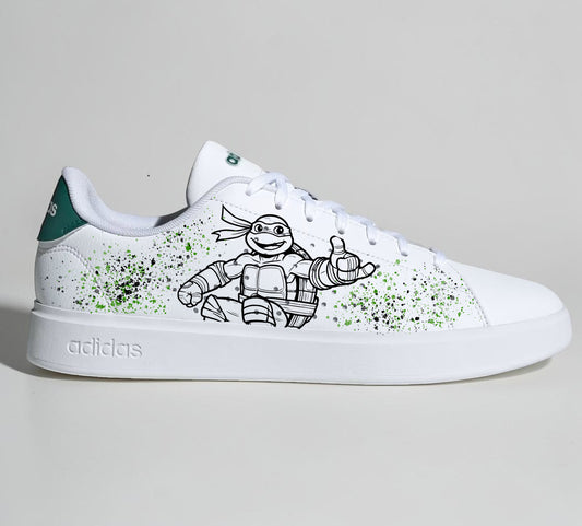 Baskets Adidas blanches personnalisées avec un dessin de Tortue Ninja et des éclaboussures de peinture verte.